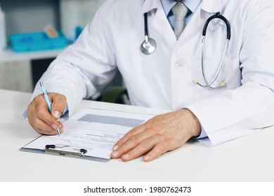 Confident Old Mature Male Doctor Physician Therapist Working At Office, Handwriting Notes. Close Up Wrinkled Male Doctor Writing Information In Medical Registration Journal