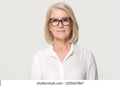 Confident older businesswoman in glasses looking at camera, middle aged senior female professional, mature lady teacher business coach head shot portrait isolated on white grey studio background