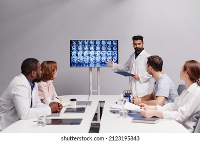 Confident Oncologist In Lab Coat Making Presentation Of Patient Mri Scan To Young Intercultural Colleagues At Meeting In Boardroom