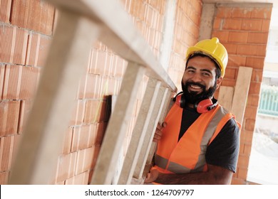 Confident People Working In Construction Site. Portrait Of Happy Hispanic Man At Work In New Housing Project. Professional Latino Worker Using Ladder And Smiling At Camera