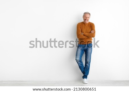 Confident Person. Portrait of cheerful casual senior man posing with folded arms standing isolated over white studio background leaning on wall with crossed hands. Male adult smiling looking at camera
