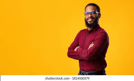 Confident Person. Portrait Of Smiling African American Man Wearing Protective Blue Light Glasses For Computer, Standing With Folded Arms Isolated Over Yellow Studio Background Wall With Copy Space