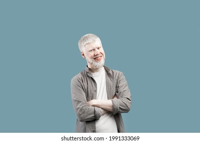 Confident Person. Smiling Albino Guy With Folded Arms Looking At Camera, Posing Isolated Over Blue Studio Background. Happy Casual Male Model Laughing