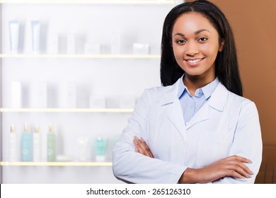 Confident Pharmacist. Beautiful Young African Woman In Lab Coat Keeping Arms Crossed And Smiling While Standing In Drugstore 