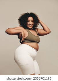 Confident plus size woman dancing in a studio, enjoying herself and having fun with her body. Happy woman in fitness clothing expressing her sense of self with body movements.