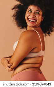 Confident plus size woman looking away with a cheerful smile while wearing underwear. Body positive woman with an Afro hairstyle embracing her natural body and curly hair.