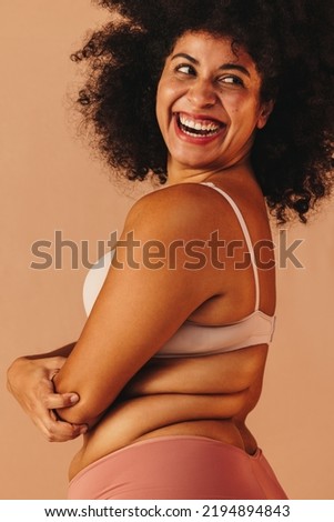 Confident plus size woman looking away with a cheerful smile while wearing underwear. Body positive woman with an Afro hairstyle embracing her natural body and curly hair.