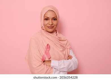 Confident portrait of a friendly Arab Muslim woman wearing a hijab and pink satin ribbon showing her support for cancer patients and survivors. Women's health care. World Breast Cancer Awareness Day. - Shutterstock ID 2036354228