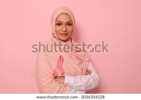 Confident portrait of a friendly Arab Muslim woman wearing a hijab and pink satin ribbon showing her support for cancer patients and survivors. Women's health care. World Breast Cancer Awareness Day.