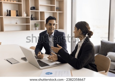 Confident positive Indian client and developer discussing online project, software project at laptop, teamwork, talking in office. Colleagues collaborating on Internet startup in office meeting room