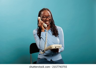 Confident positive young adult woman answering customer calling for consultancy. Happy smiling landline telephone operator having a conversation on wired phone on blue background.
