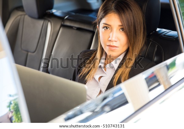 Confident and powerful\
businesswoman riding a car on a business trip and using a laptop\
computer