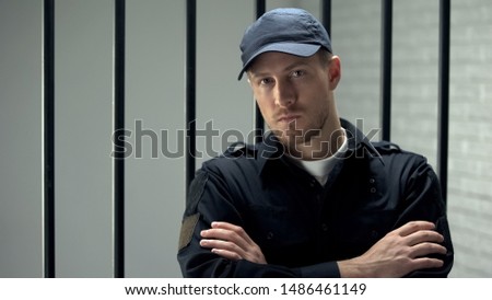 Confident prison security guard looking to camera standing near cell, profession