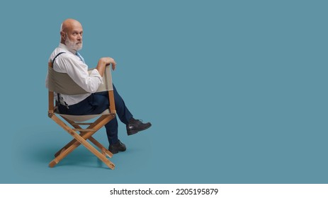 Confident Professional Filmmaker Sitting On The Director's Chair And Looking At Camera: Drama School, Video Production And Film Industry Concept, Blank Copy Space