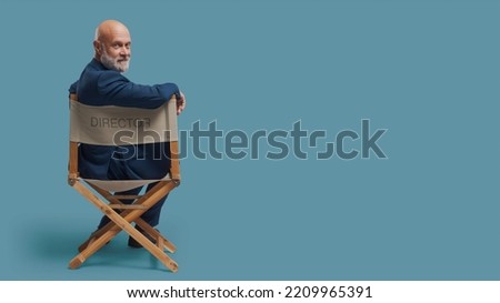 Confident professional filmmaker sitting on the director's chair and looking at camera: drama school, video production and film industry concept, blank copy space