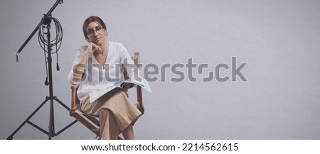Confident professional filmmaker sitting on the director's chair and holding a play script: drama school and film industry concept, copy space