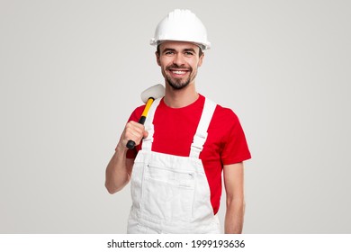 Confident professional male contractor in workwear and hardhat with hammer in hand smiling and looking at camera against white background