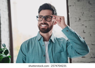 Confident professional man smiling while adjusting his glasses in a modern indoor workspace