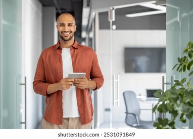 Confident professional in modern office holding tablet, smiling. Wearing casual business attire, exhibiting success and positivity. Ideal image for business concept, workplace, and technology. - Powered by Shutterstock