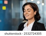 Confident professional woman in office setting practicing mindfulness with serene expression. Eyes closed, smiling softly, embracing peace, tranquility, stress relief, mental wellness.