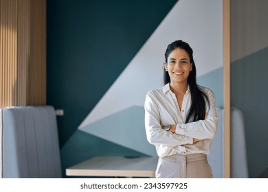 Confident professional young latin business woman company employee, lady executive manager, female worker or entrepreneur looking at camera standing arms crossed in modern office, portrait.