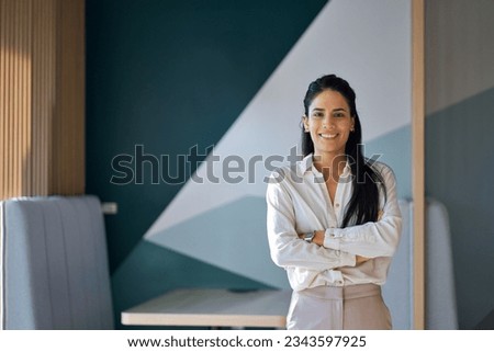 Confident professional young latin business woman company employee, lady executive manager, female worker or entrepreneur looking at camera standing arms crossed in modern office, portrait.