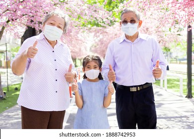 Confident And Protect On Outdoor Park With Asian Family. Happy Grandfather And Grandmother And Kid With Face Mask To Protect Coronavirus Pandemic.