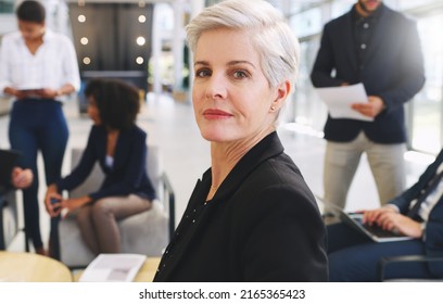 Confident And Proud Of My Team. Cropped Portrait Of An Attractive Mature Businesswoman Sitting While Her Colleagues Work Behind Her In The Office.