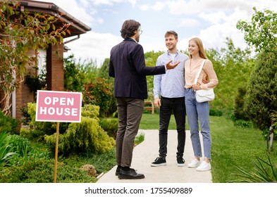 Confident Realtor Showing House For Sale To Newlywed Young Couple, Outside