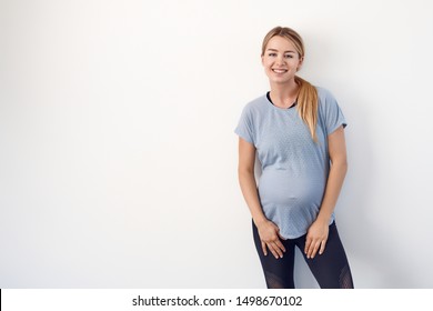 Confident relaxed attractive young pregnant woman standing with folded arms resting on her bare baby belly looking at the camera with a friendly smile over white with copy space