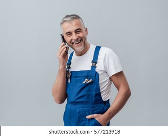 Confident repairman and plumber having a phone call with his smartphone and smiling