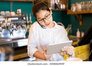 Confident Restaurant Manager Answering Phone While Adding Information About Table Reservation In Cafe. Positive Young Asian Female Coffee Shop Owner Solving Urgent Issues. Small Business Concept