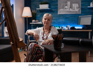 Confident retired sketch artist posing inspired in home hobby art studio sitting in wheelchair in front of easel with canvas. Portrait of senior painter holding pencil in drawing workshop. - Powered by Shutterstock