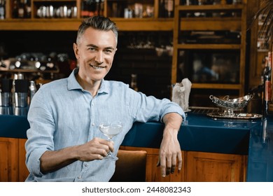 Confident rich middle-aged mature wealthy businessman chilling relaxing drinking enjoying cocktail sparkling wine at the bar counter after work - Powered by Shutterstock