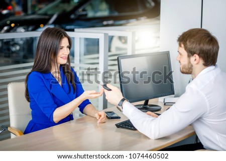 Confident salesman handing over car keys to a female customer completing profitable deal