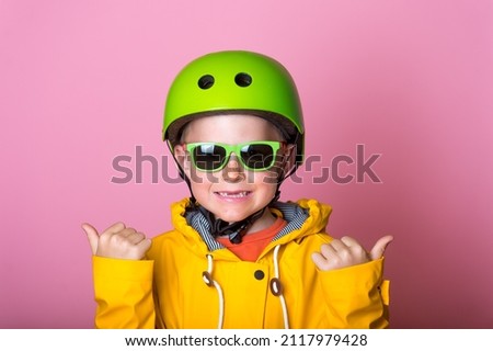Confident school boy in full sport protect equipment with thumbs up. Blond kid safety helmet and sunglasses. Child in yellow bright clothes isolated on pink