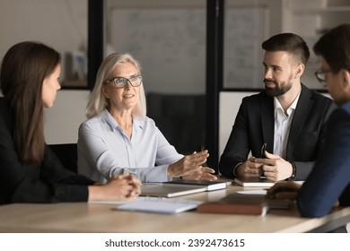 Confident senior business professional woman speaking to colleagues on corporate meeting, giving ideas, solutions for marketing strategy, discussing project management, brainstorming - Powered by Shutterstock