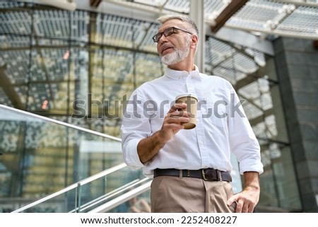 Confident senior mature old successful business man leader, smiling mid aged senior professional businessman executive ceo wearing white shirt holding coffee looking away thinking standing outdoor.