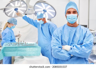 Confident senior physician with crossed arms in the operating room with team in the background - Powered by Shutterstock