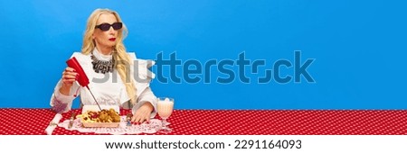 Confident senior woman putting ketchup on fried chicken and potatoes against blue background. Food pop art photography. Complementary colors. Concept of food, creativity. Banner. Copy space for ad