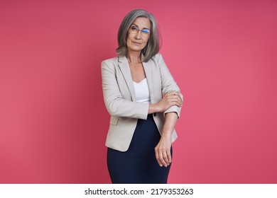 Confident Senior Woman Rolling Up Sleeve On Her Jacket While Standing Against Pink Background