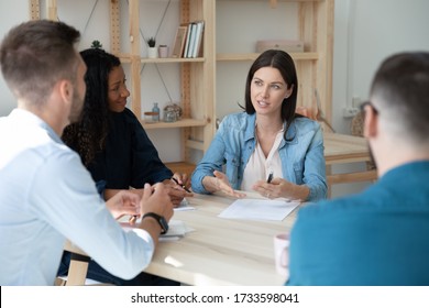 Confident Serious Businesswoman Telling Diverse Employees About Project Sit At Table In Boardroom At Company Meeting. Female Mentor Discuss Business With African American Woman And Colleagues.