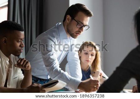 Confident serious male ceo executive manager in glasses analyzing financial paper documents at briefing meeting with young diverse colleagues or developing company growth strategy together in office.