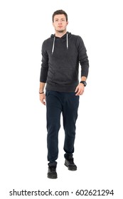 Confident Serious Man In Sweatshirt And Tracksuit Walking Towards Camera. Full Body Length Portrait Over White Studio Background.