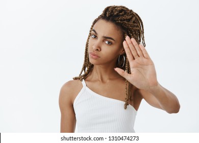 Confident serious-looking displeased and annoyed african american woman with dreadlocks raising palms to decline and say no demanding person stop shooting being irritated over gray wall - Powered by Shutterstock