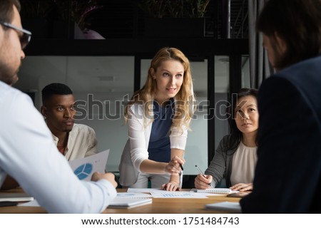 Confident skilled businesswoman explain marketing data paper report financial results analysis to multi-ethnic colleagues, company staff gathered at meeting brainstorming thinking strategizing concept