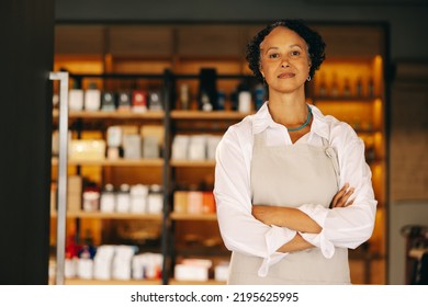 Confident Small Business Owner Looking At The Camera While Standing At The Entrance Of Her Grocery Store With Her Arms Crossed. Mature Entrepreneur Running A Trendy Convenience Store.