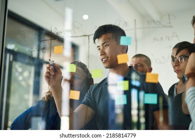 Confident, Smart And Creative Team Brainstorming A Strategy Idea And Writing On Sticky Notes On A Transparent Board In A Meeting. Diverse Group Planning And Working In Close Collaboration Together