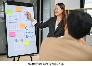 Confident And Smart Young Asian Businesswoman Or Female Financial Analyst Presenting Her Financial Data Informations To Her Board Members In The Meeting.