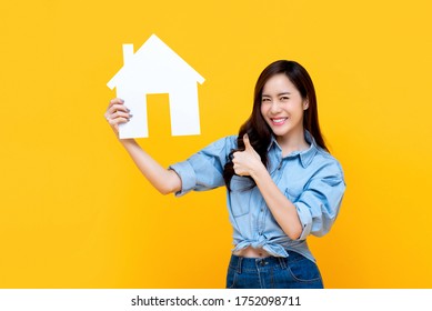 Confident Smiling  Beautiful Asian Woman Holding Up  Paper House With Thumbs Up Gesture Isolated On Yellow Studio Background